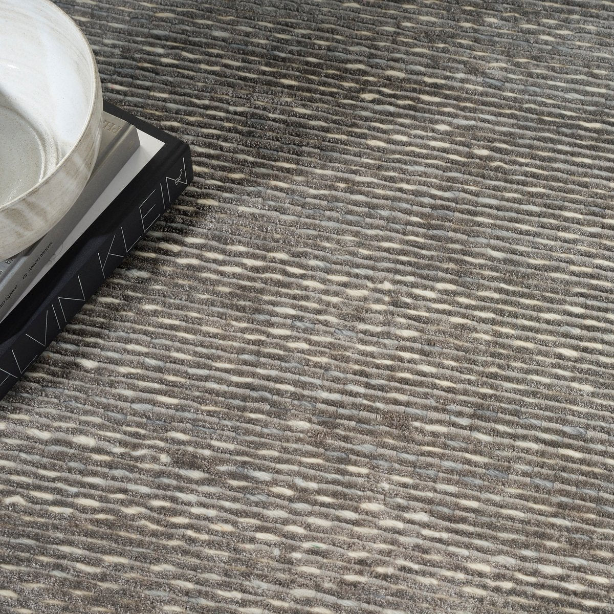 Grey textured rug with subtle horizontal striations and mottled appearance throughout